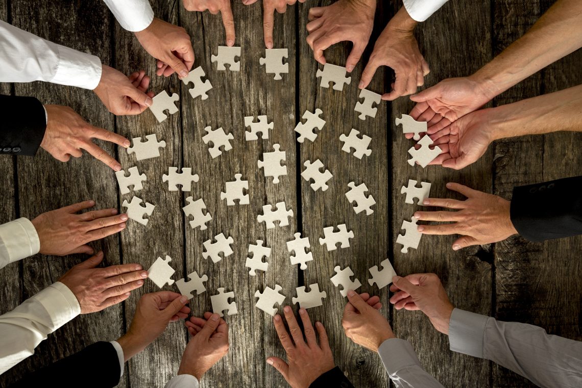 Teamwork Concept - High Angle View of Businessmen Hands Forming Circle and Holding Puzzle Pieces on Top of a Rustic Wooden Table.